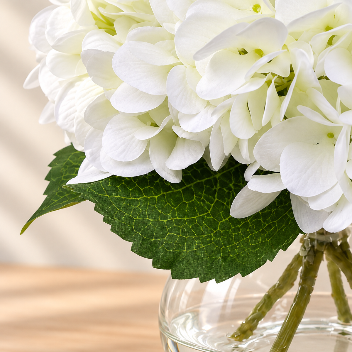 White hydrangea arrangement in glass vase with faux water — leaf detail